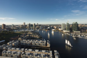 Arial color photo of Baltimore's Inner Harbor, with sailboats and the Baltimore skyline in the background.