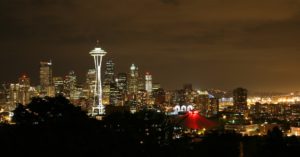 A photo of the Seattle, WA, city skyline lit up at night, with a deep orange sky.